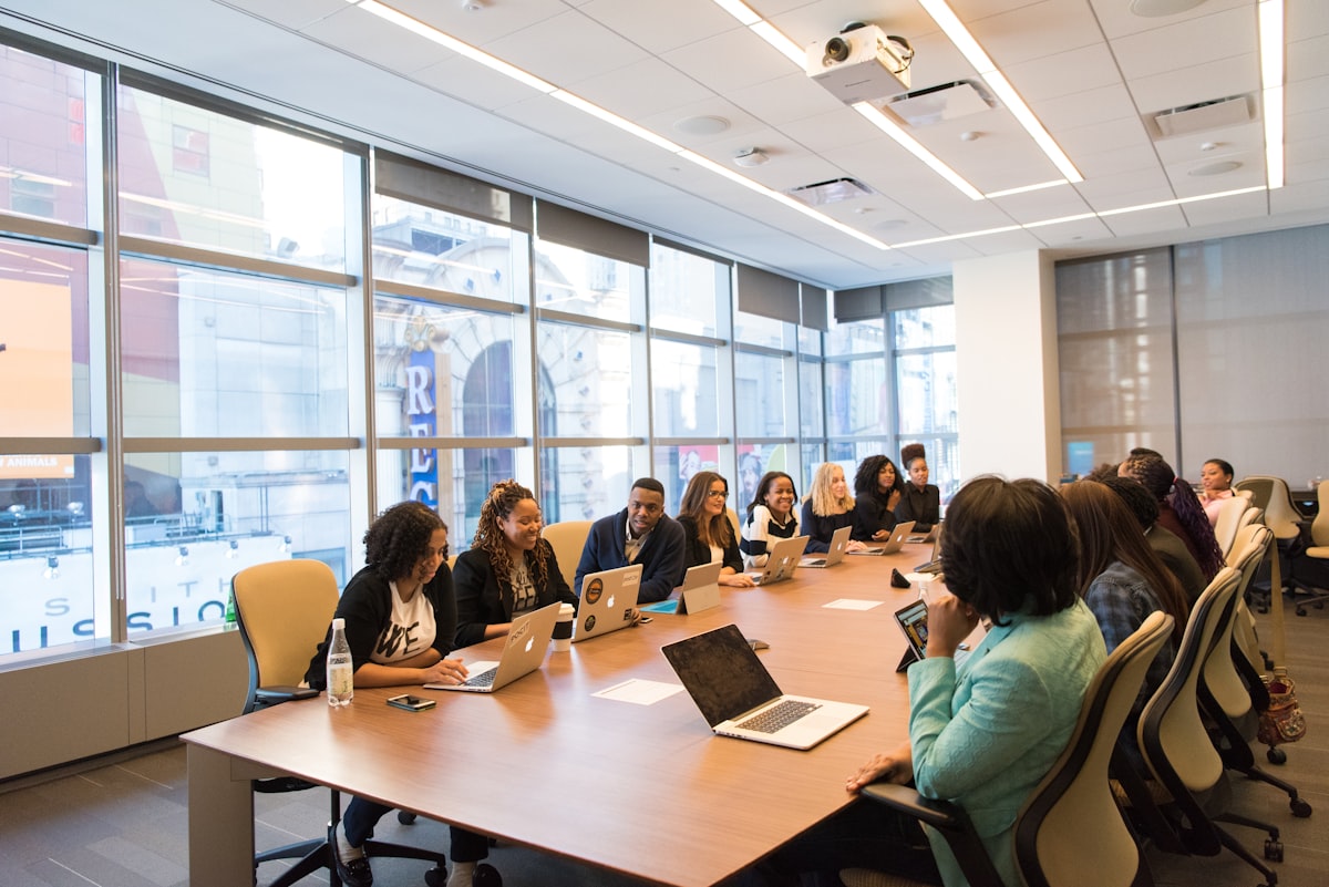 Diverse editorial team gathered around a meeting table with laptops and bright windows